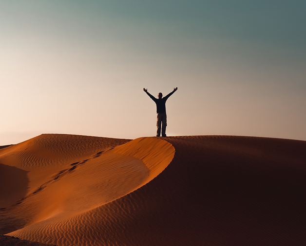 두바이 아라비아해 크루즈 - 사막의 모래언덕에서 두 팔을 벌리고 서 있는 실루엣과 황금빛 사막 풍경